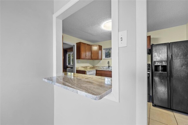 kitchen featuring black fridge with ice dispenser, kitchen peninsula, light tile patterned floors, a textured ceiling, and sink