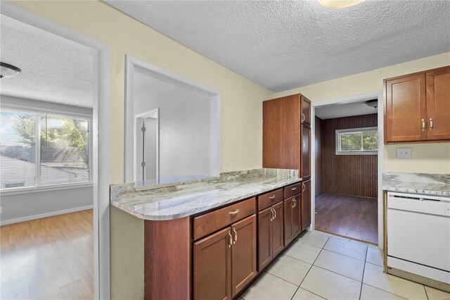 kitchen featuring light hardwood / wood-style flooring, dishwasher, a textured ceiling, and light stone countertops