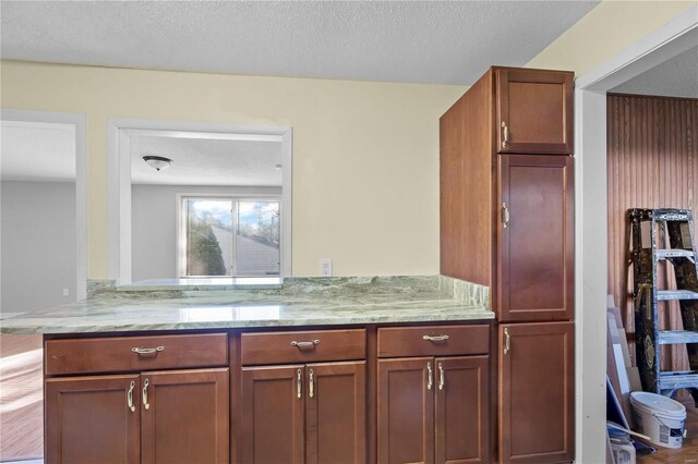 kitchen featuring a textured ceiling, kitchen peninsula, and light stone countertops