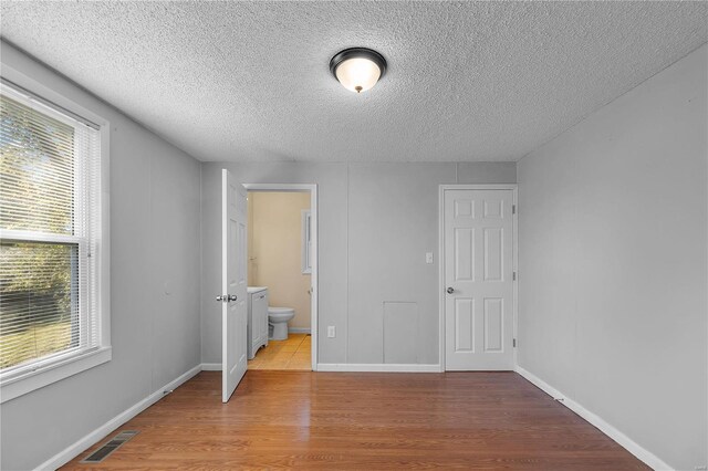 unfurnished bedroom with multiple windows, a textured ceiling, connected bathroom, and light hardwood / wood-style flooring