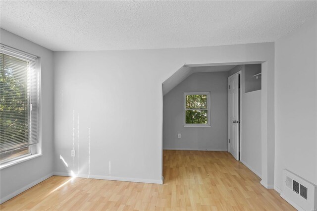 additional living space featuring light wood-type flooring, a wealth of natural light, and a textured ceiling