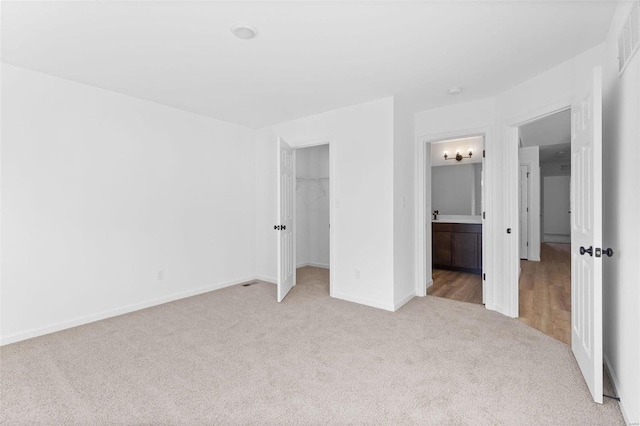 unfurnished bedroom featuring connected bathroom, light carpet, a walk in closet, and a closet