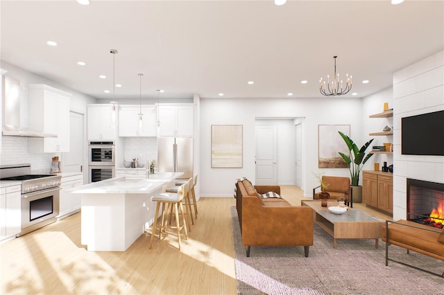 interior space featuring high end appliances, a fireplace, pendant lighting, light wood-type flooring, and a kitchen island with sink