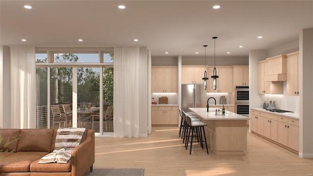 kitchen with appliances with stainless steel finishes, hanging light fixtures, light hardwood / wood-style floors, and an island with sink