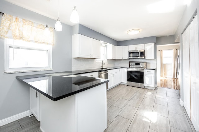 kitchen featuring pendant lighting, sink, white cabinetry, stainless steel appliances, and kitchen peninsula