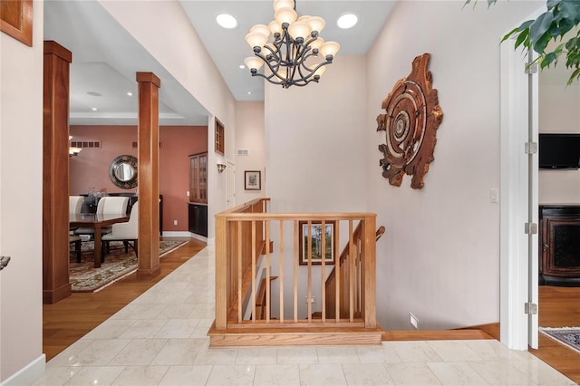 hall with an inviting chandelier, light wood-type flooring, and ornate columns