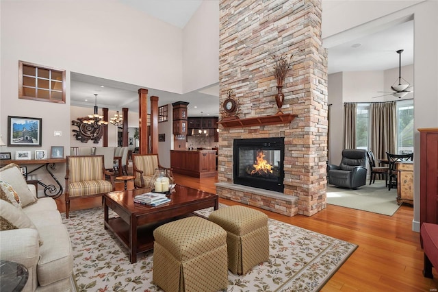 living room featuring ceiling fan with notable chandelier, a towering ceiling, light hardwood / wood-style floors, and a stone fireplace