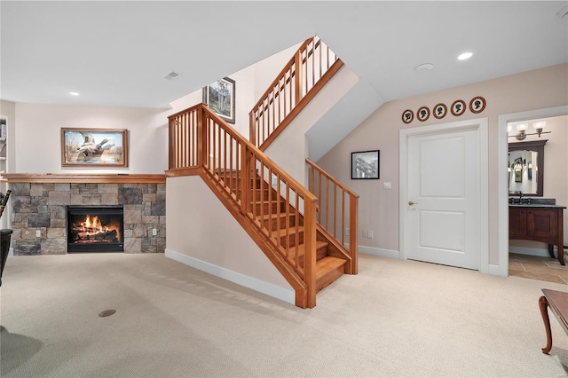 stairway with carpet floors and a stone fireplace