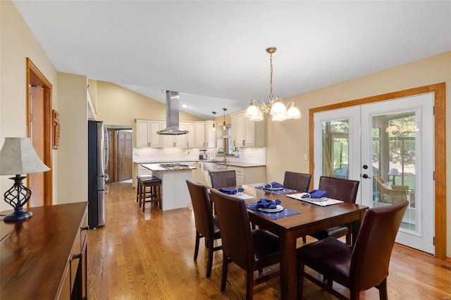 dining area with lofted ceiling, light wood-type flooring, french doors, sink, and a notable chandelier