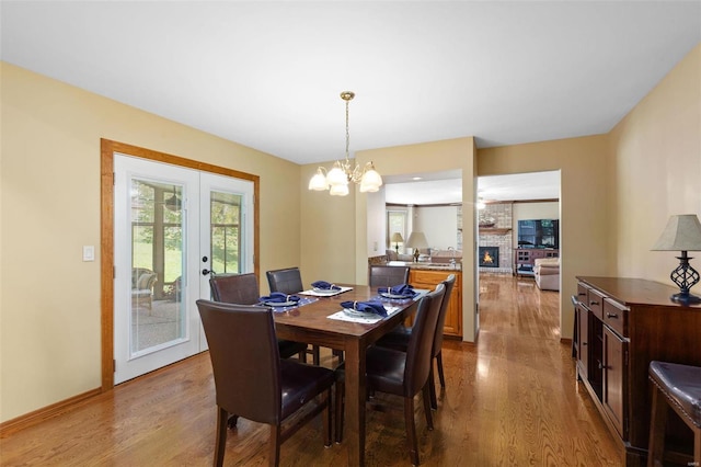 dining room with a notable chandelier, a fireplace, french doors, and light hardwood / wood-style flooring