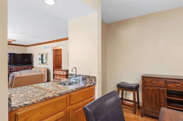 interior space featuring ornamental molding, light hardwood / wood-style flooring, stone counters, and sink