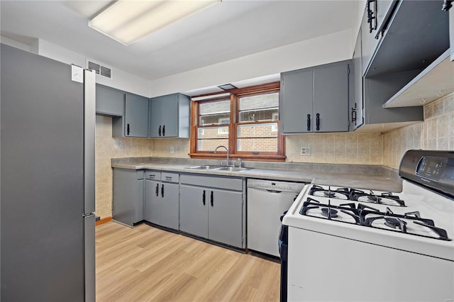 kitchen with decorative backsplash, white appliances, sink, gray cabinets, and light hardwood / wood-style floors