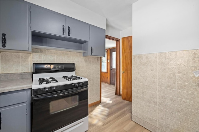 kitchen featuring gray cabinets, white gas stove, light hardwood / wood-style floors, and tile walls