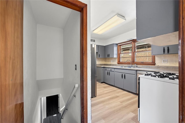 kitchen with gray cabinetry, backsplash, sink, light hardwood / wood-style flooring, and white gas range