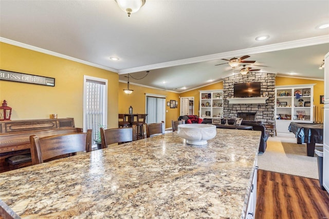 kitchen featuring ceiling fan, crown molding, light stone counters, lofted ceiling, and a fireplace