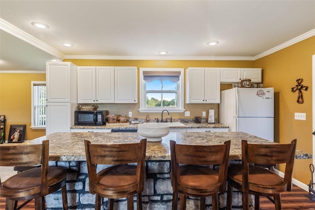 kitchen featuring a kitchen breakfast bar, ornamental molding, white fridge, and white cabinetry