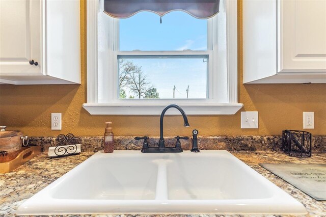 room details featuring light stone counters, sink, and white cabinets