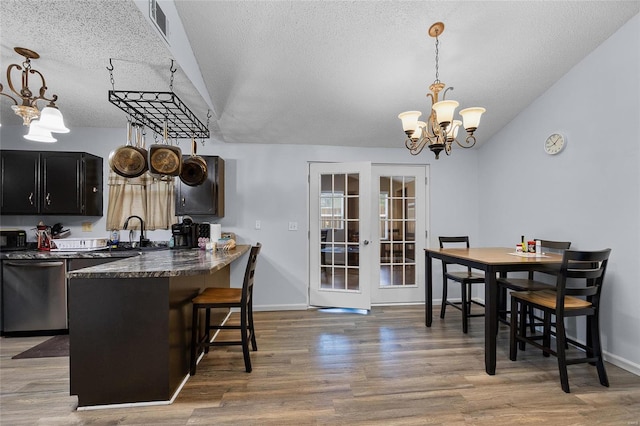 kitchen featuring pendant lighting, dishwasher, hardwood / wood-style flooring, a textured ceiling, and a kitchen bar