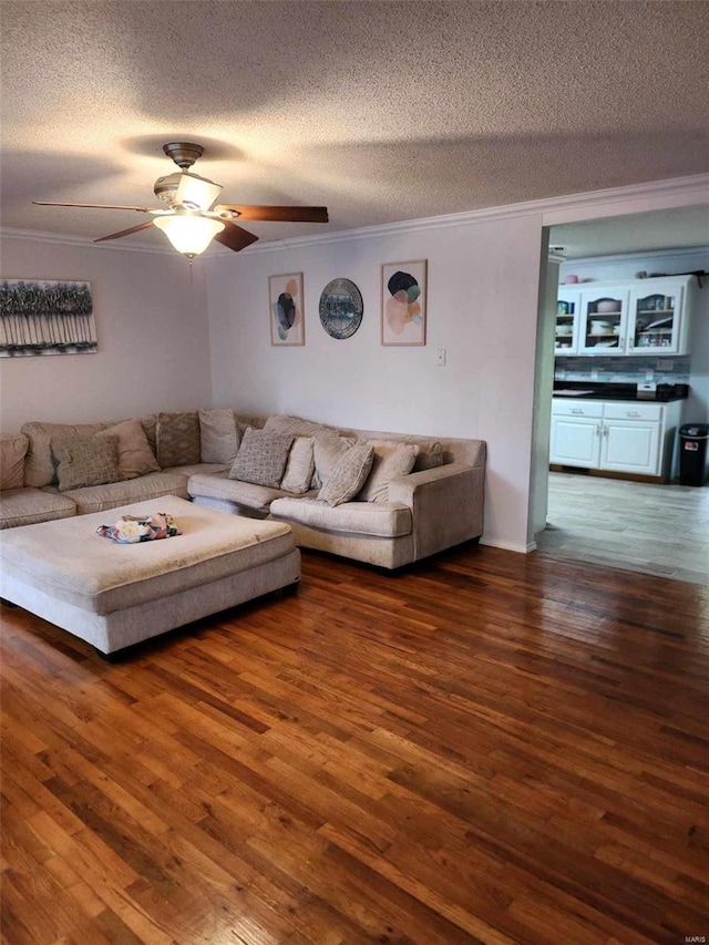 unfurnished living room with a textured ceiling, ornamental molding, dark wood-type flooring, and ceiling fan