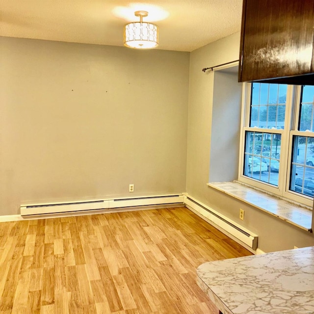 empty room with a textured ceiling, light hardwood / wood-style floors, and a baseboard heating unit