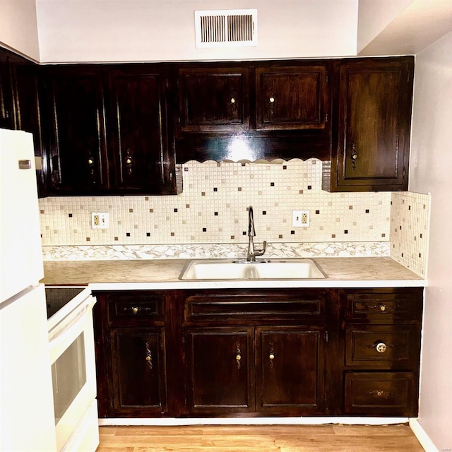 kitchen with dark brown cabinets, sink, light hardwood / wood-style flooring, decorative backsplash, and white appliances