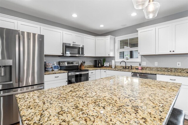 kitchen featuring light stone counters, a center island, white cabinets, appliances with stainless steel finishes, and decorative light fixtures