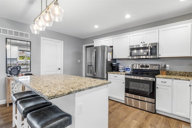 kitchen with white cabinets, appliances with stainless steel finishes, hanging light fixtures, and light hardwood / wood-style floors