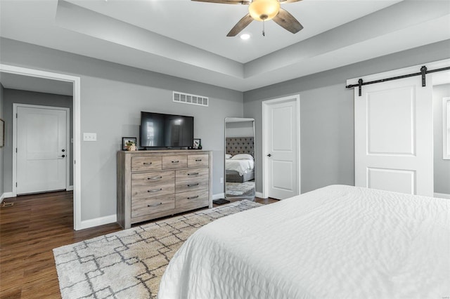 bedroom with a barn door, dark hardwood / wood-style floors, and ceiling fan