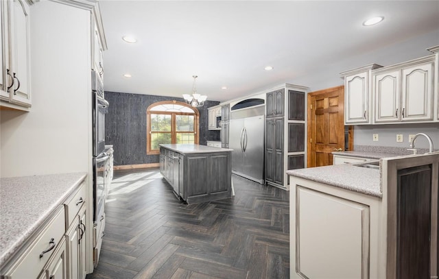 kitchen featuring stainless steel built in fridge, pendant lighting, dark parquet flooring, a center island, and a notable chandelier