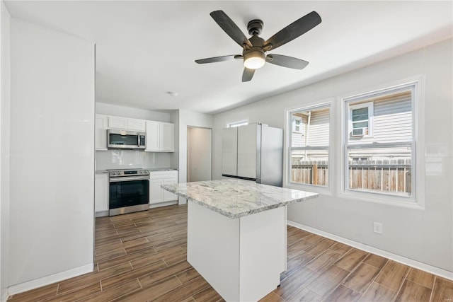 kitchen with appliances with stainless steel finishes, white cabinetry, dark wood-type flooring, light stone counters, and ceiling fan