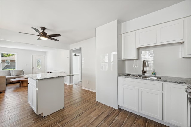 kitchen with light stone counters, ceiling fan, sink, white cabinetry, and hardwood / wood-style floors