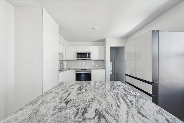 kitchen featuring light stone countertops, stainless steel appliances, and white cabinetry