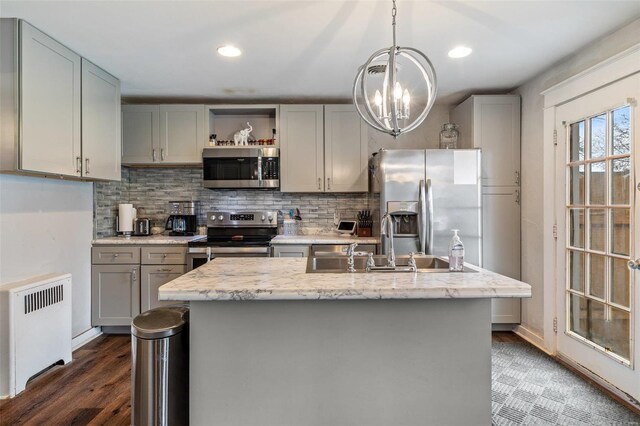 kitchen featuring gray cabinets, an island with sink, radiator heating unit, and stainless steel appliances