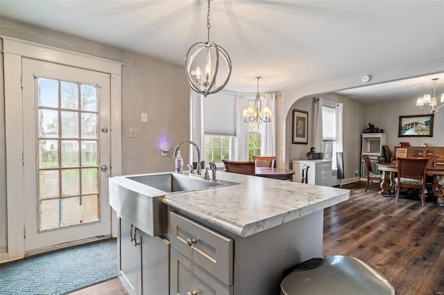 kitchen featuring dark wood-type flooring, a kitchen island with sink, a notable chandelier, decorative light fixtures, and a healthy amount of sunlight