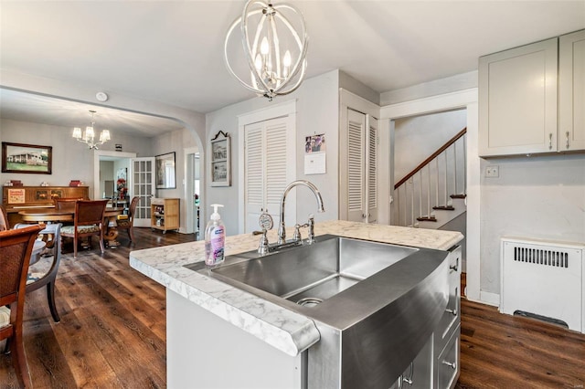 kitchen featuring radiator, an inviting chandelier, a center island with sink, and dark hardwood / wood-style floors