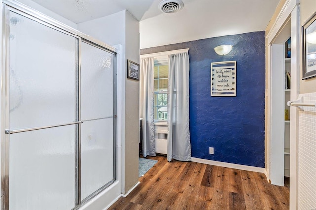 bathroom with radiator heating unit, a shower with shower door, and hardwood / wood-style floors