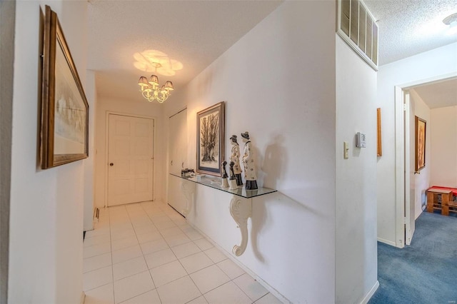 hall featuring a textured ceiling, light tile patterned flooring, and a chandelier