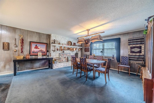 dining room with dark carpet, wood walls, a textured ceiling, and a stone fireplace