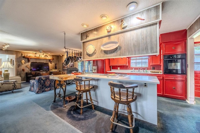 kitchen with dark colored carpet, kitchen peninsula, black oven, and plenty of natural light