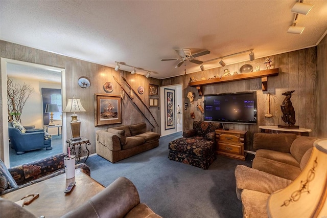 living room featuring rail lighting, carpet floors, wood walls, a textured ceiling, and ceiling fan