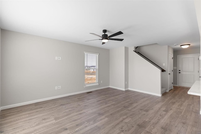 unfurnished living room with light wood finished floors, baseboards, stairway, and a ceiling fan