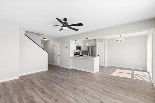 unfurnished living room with visible vents, light wood-style flooring, baseboards, a sink, and ceiling fan with notable chandelier