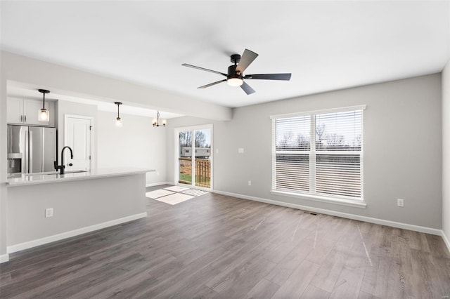 unfurnished living room with baseboards, dark wood-style floors, a sink, and ceiling fan with notable chandelier