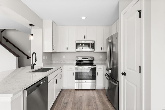 kitchen with a peninsula, light wood finished floors, light stone countertops, appliances with stainless steel finishes, and a sink