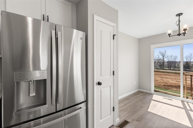 kitchen featuring white cabinetry, pendant lighting, light hardwood / wood-style flooring, stainless steel refrigerator with ice dispenser, and a notable chandelier