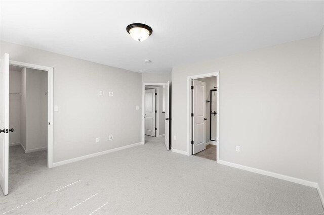 unfurnished bedroom with a spacious closet, a closet, light colored carpet, and ensuite bathroom