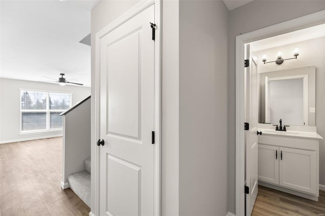 hallway featuring baseboards, stairs, a sink, and light wood finished floors