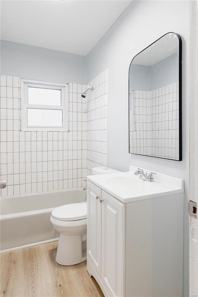 full bathroom with hardwood / wood-style floors, tiled shower / bath, vanity, and toilet