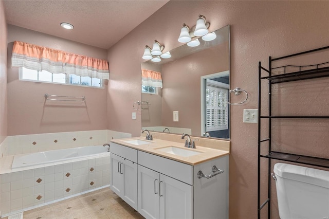 bathroom with a textured ceiling, tiled tub, vanity, and toilet