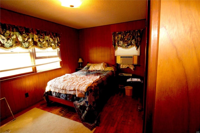 bedroom with cooling unit, hardwood / wood-style flooring, wood walls, and a textured ceiling